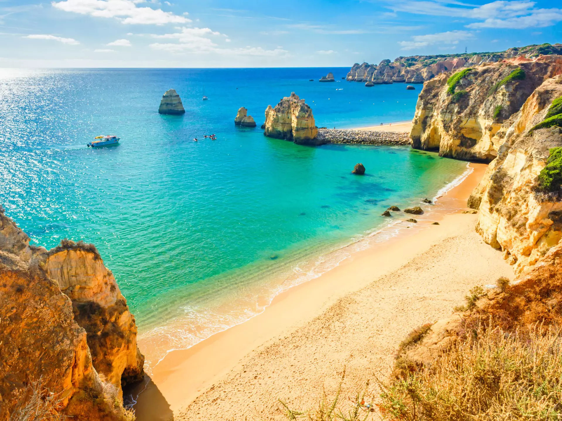 A sandy beach with blue-green water and large rock formations on its shore
