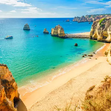 A sandy beach with blue-green water and large rock formations on its shore