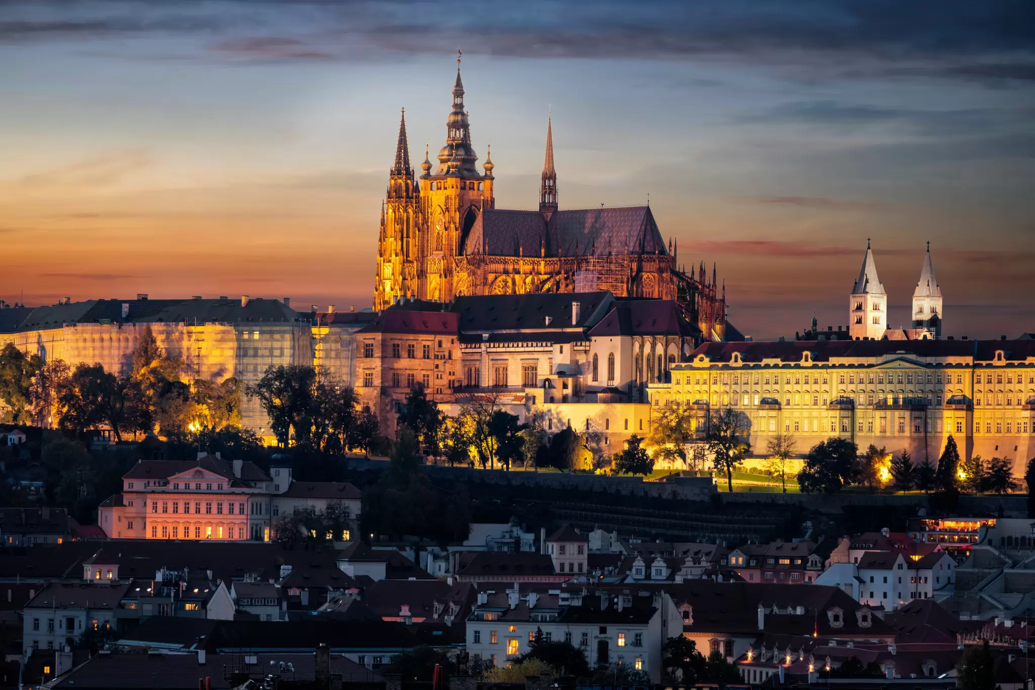 A castle at the top of a hill in a city is illuminated in the evening light, Prague