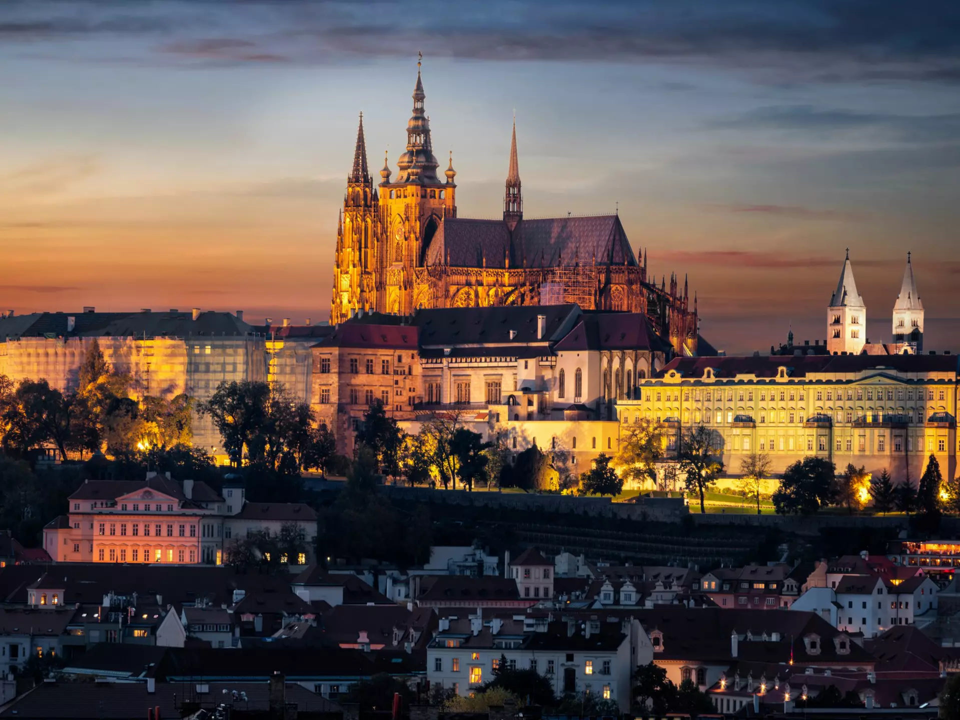 A castle at the top of a hill in a city is illuminated in the evening light, Prague