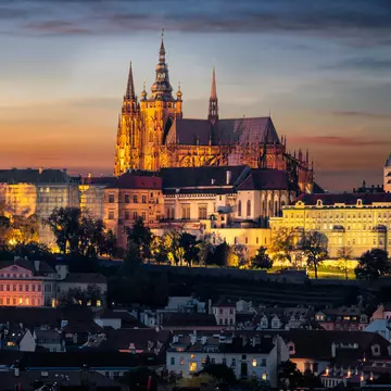 A castle at the top of a hill in a city is illuminated in the evening light, Prague