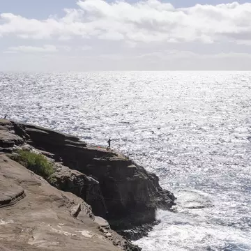 A fisherman casting a line from the cliffs at Spitting Caves, East Oahu, Hawaii
