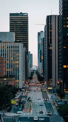 Narrow view of tall glass skyscrapers lining either side of a busy city street.