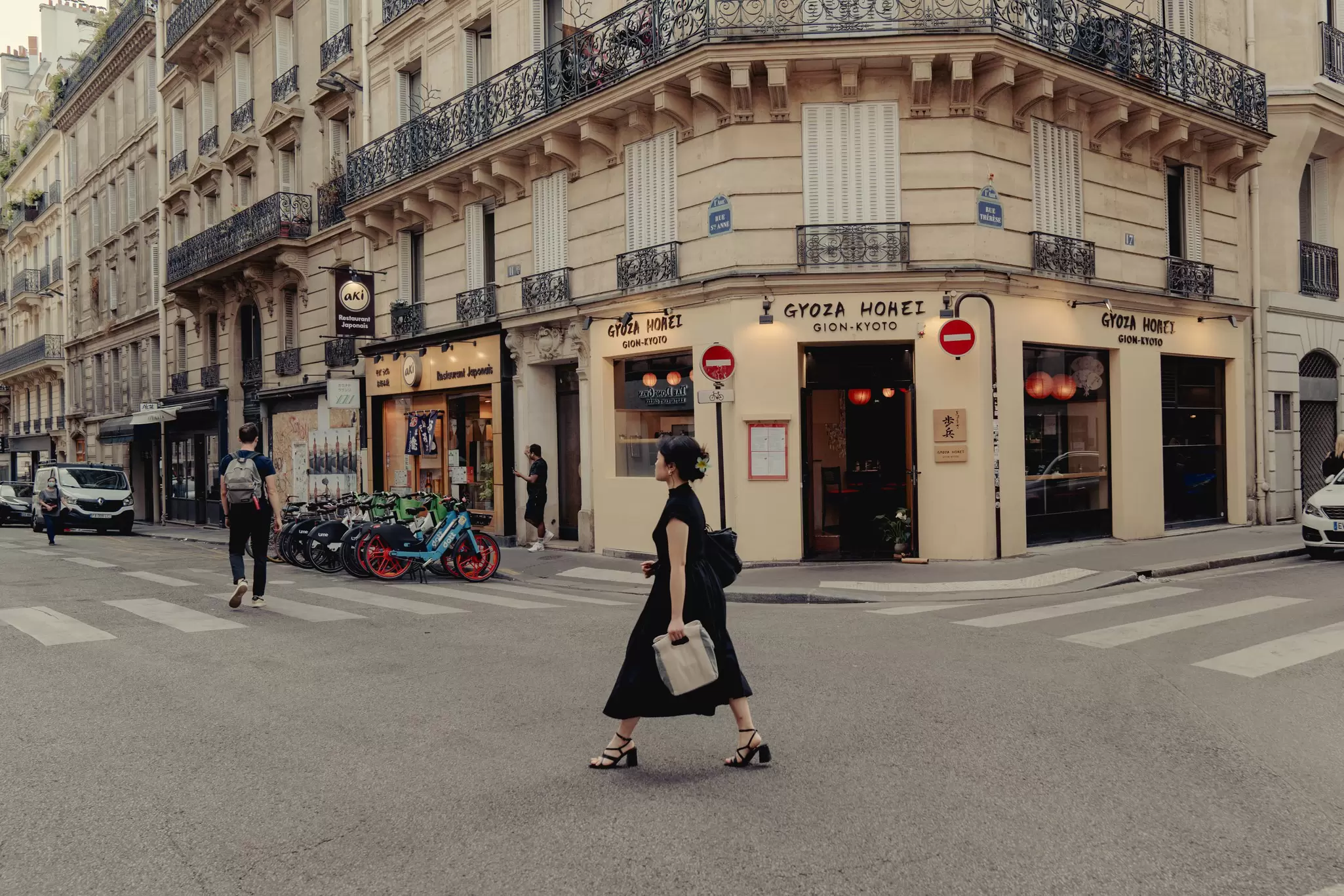 A woman in black carrying a bag walks purposefully on Rue Sainte-Anne, home to Little Tokyo in Paris, France. 