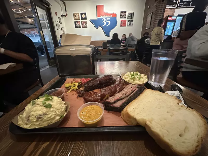 Tray of food with sausage, brisket, pork ribs, bread and potato salad. 