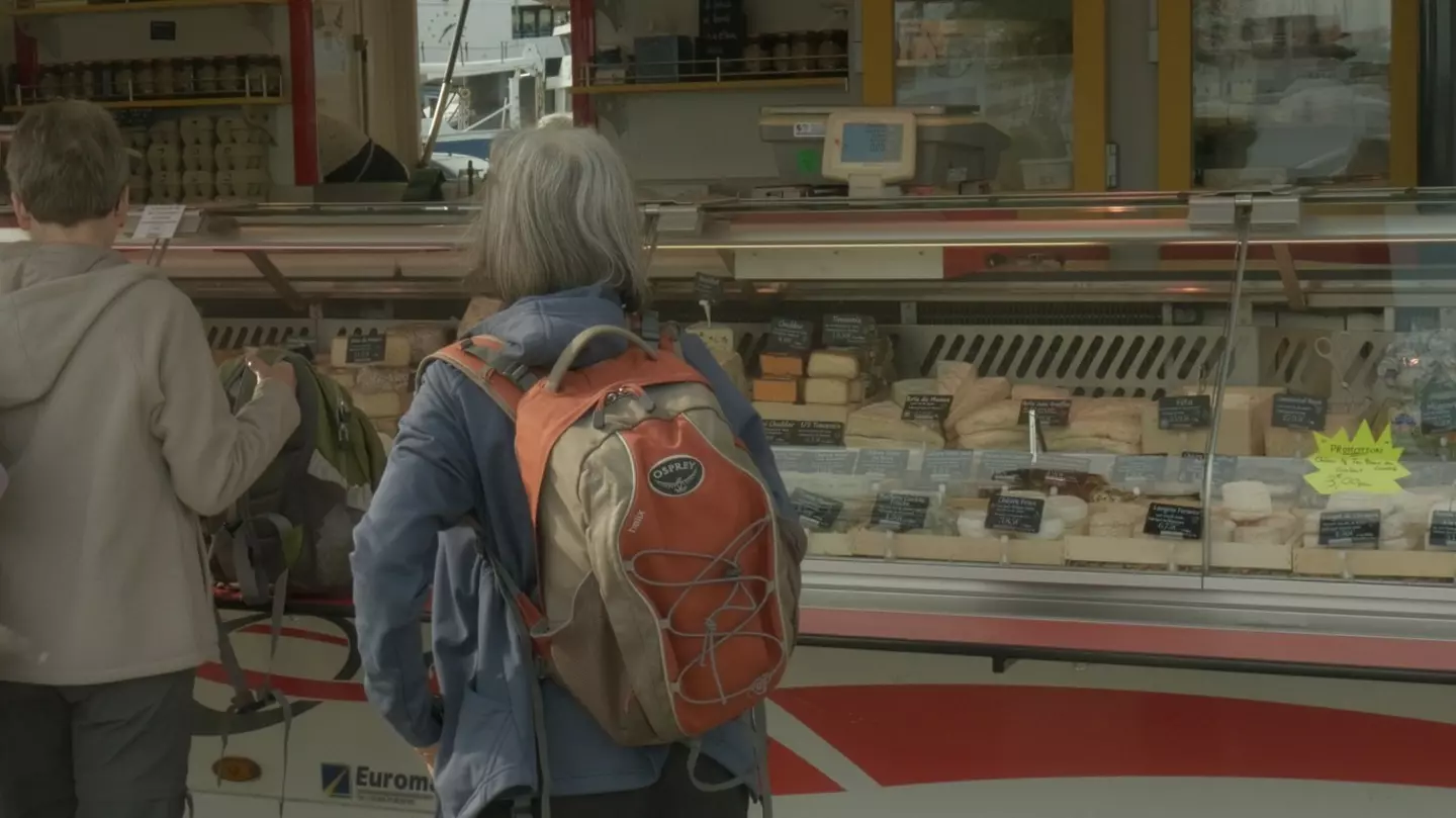 A woman standing as she waits to order cheese at the market.