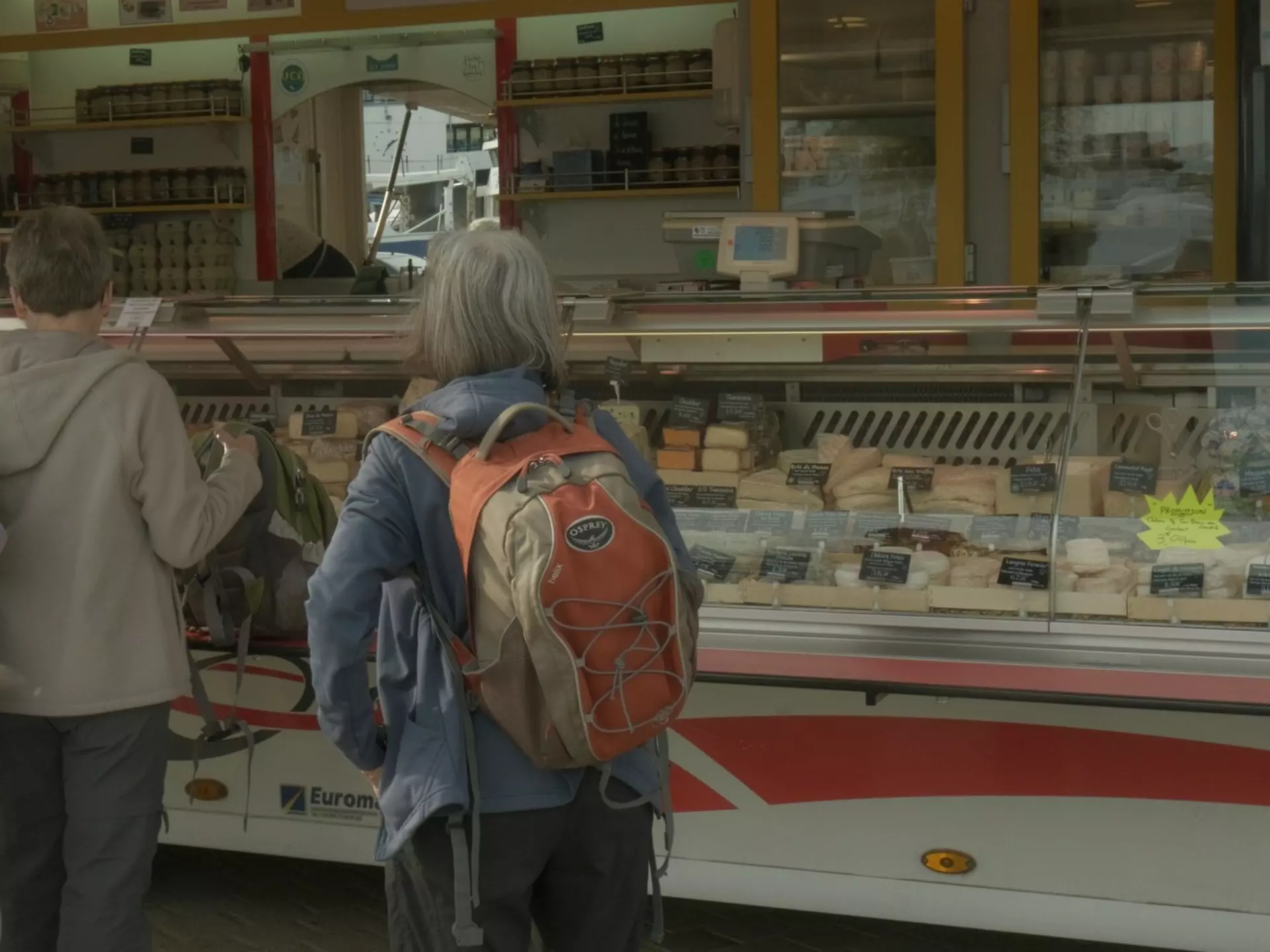 A woman standing as she waits to order cheese at the market.