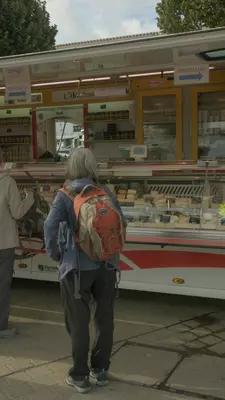 A woman standing as she waits to order cheese at the market.