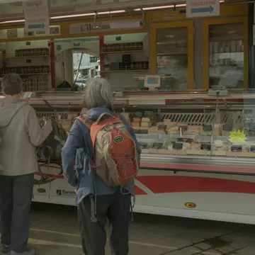 A woman standing as she waits to order cheese at the market.