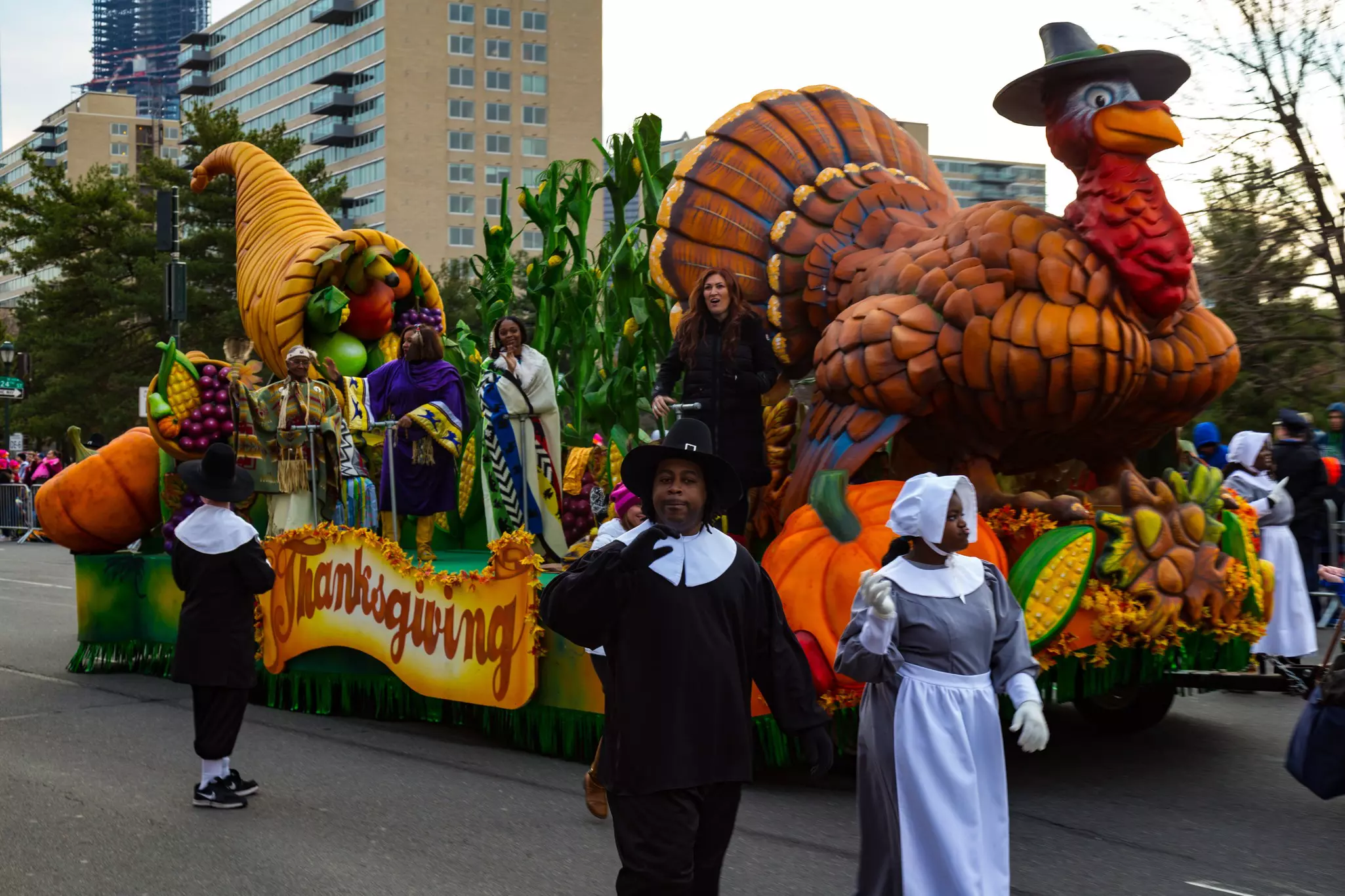 People dressed as pilgrims march alongside a turkey float in an annual Thanksgiving Day parade in a city.
