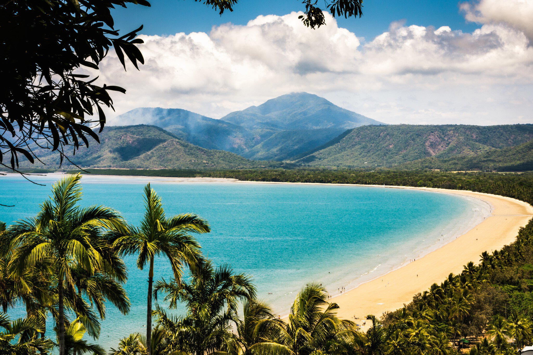 Trinity Bay Lookout in Port Douglas, Queensland, Australia.  Tropical beach with smoke from bush fire burning in the hills behind. Palm trees, clean beach sand with people swimming.