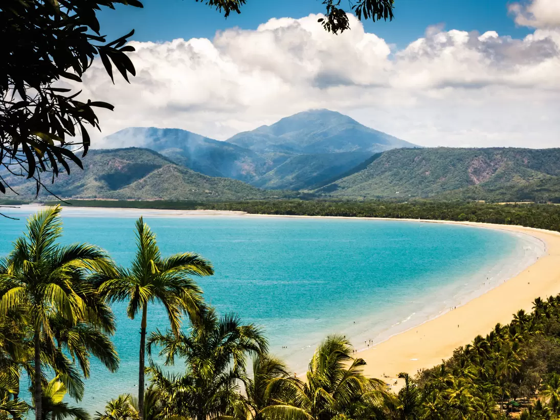 Trinity Bay Lookout in Port Douglas, Queensland, Australia.  Tropical beach with smoke from bush fire burning in the hills behind. Palm trees, clean beach sand with people swimming.