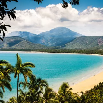 Trinity Bay Lookout in Port Douglas, Queensland, Australia.  Tropical beach with smoke from bush fire burning in the hills behind. Palm trees, clean beach sand with people swimming.
