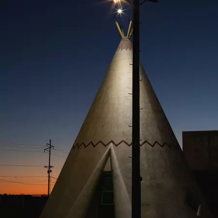 A pink, orange and deep blue sunset behind a teepee illuminated by a single street light