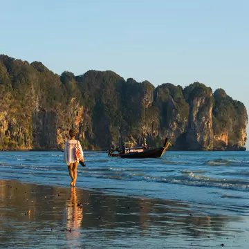 Woman walking along Ao Nang beach at sunset in Krabi, Thailand.