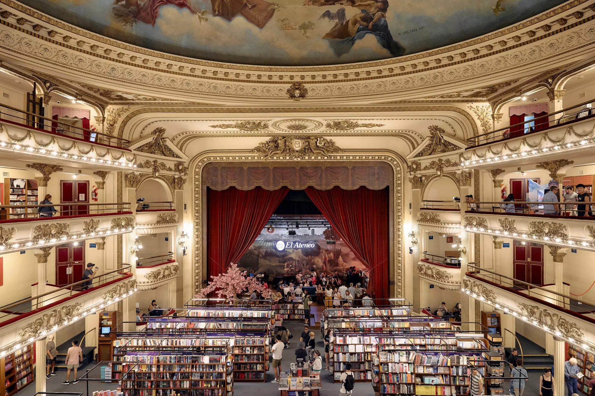 Shelves of books under a painted domed ceiling; a stage with red curtains is at the far end.