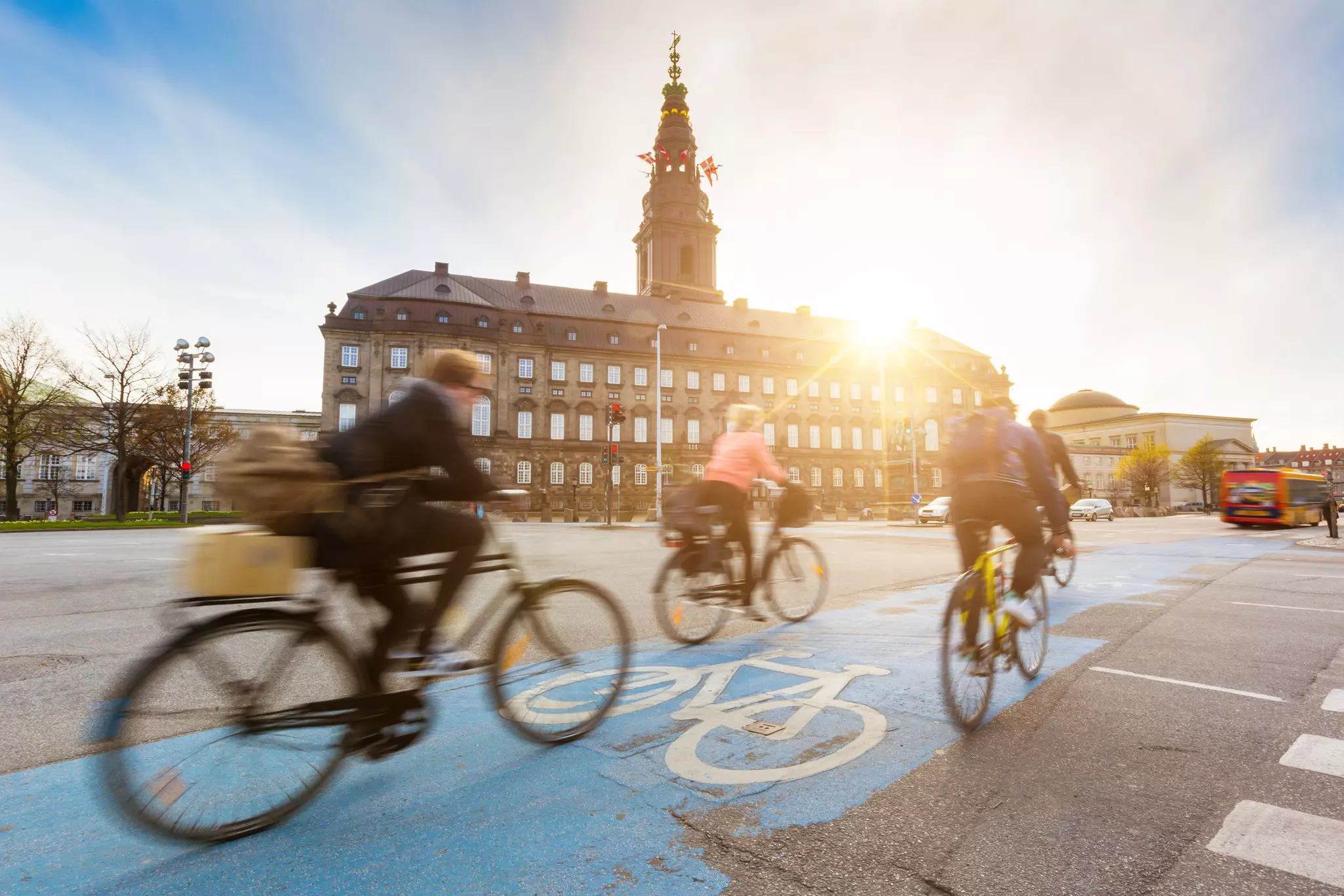 Blurred people going by bike in Copenhagen, with Christiansborg palace on background.