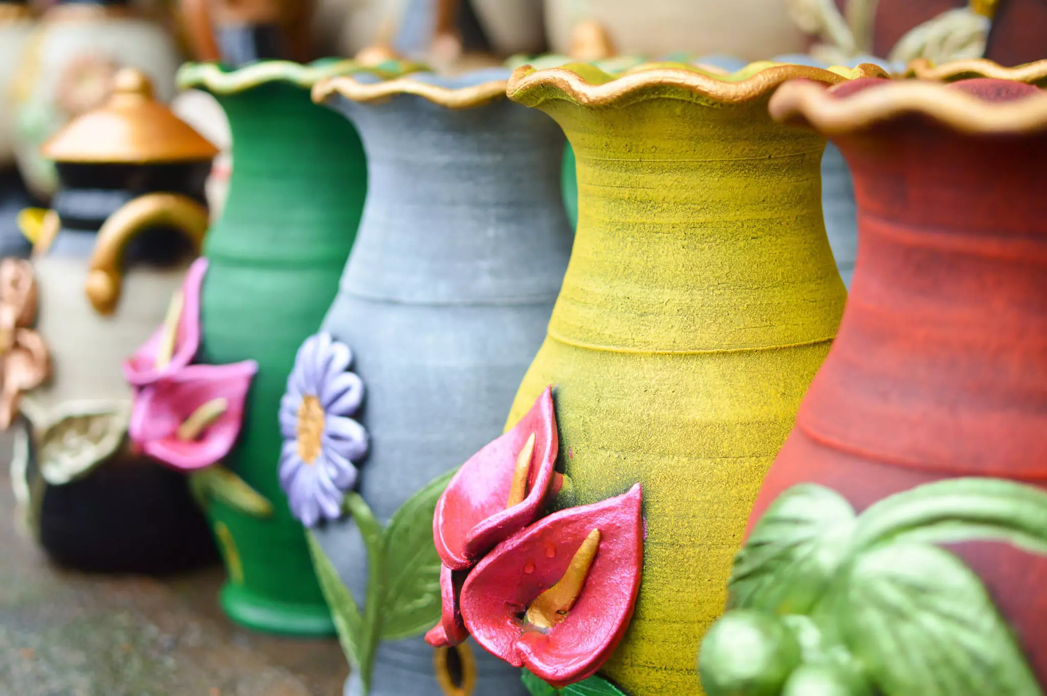 Ceramic pots in pastel colors decorated with flower sculptures.