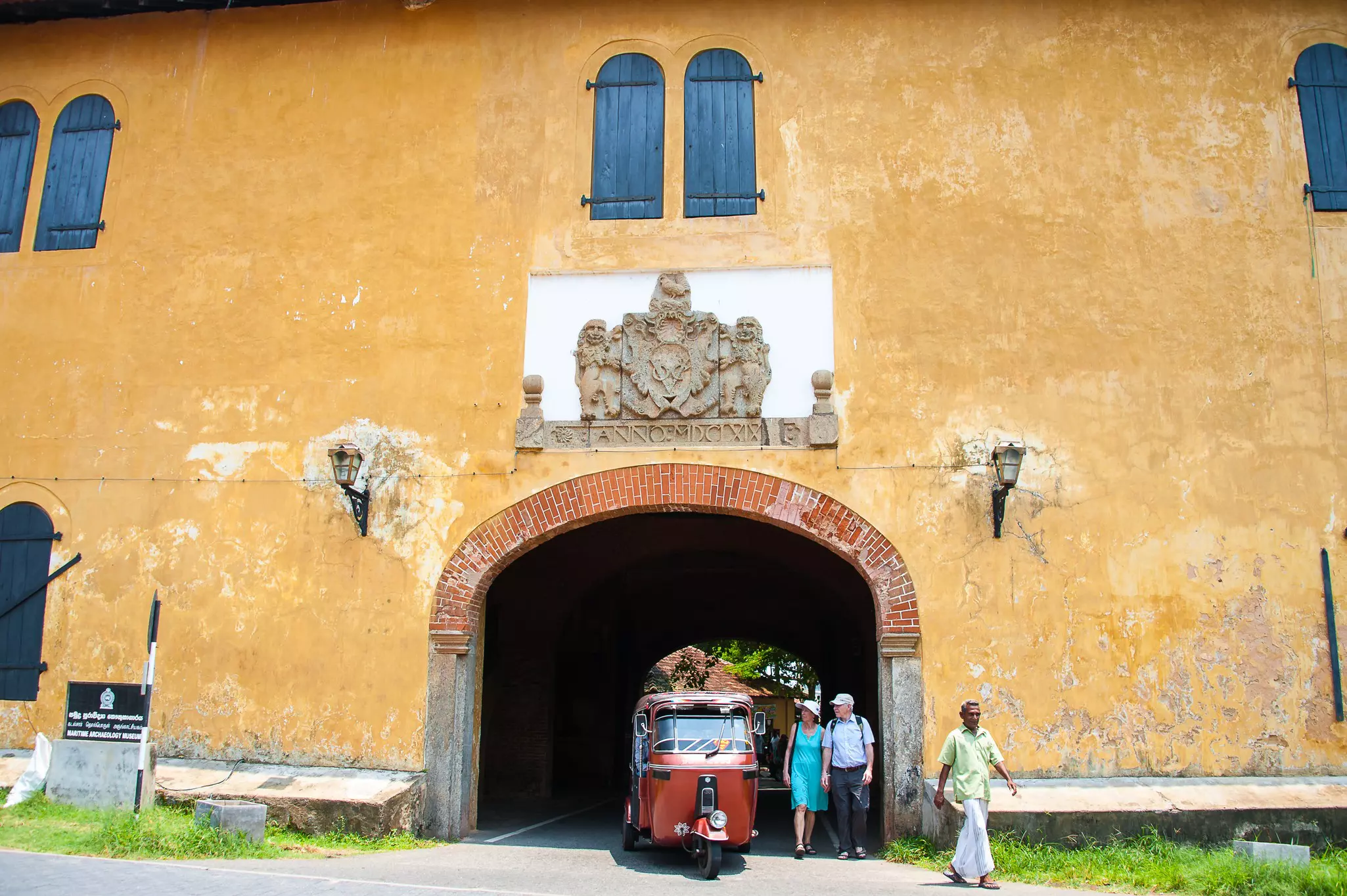 A small motorized three-wheel vehicle drives through a city gateway as people walk by