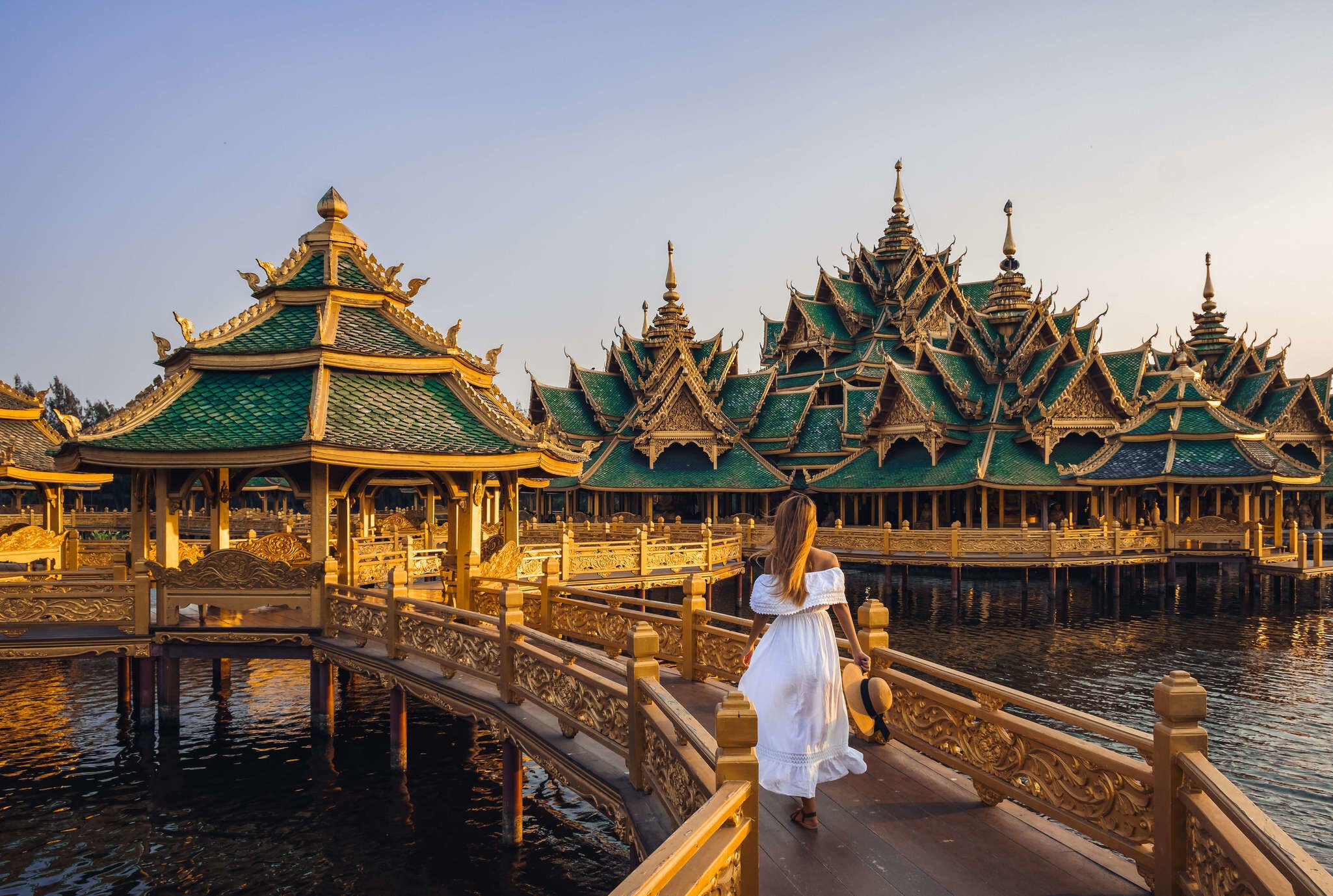 Woman walking on a bridge to Buddhist temple in Thailand during sunset.