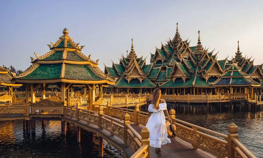 Woman walking on a bridge to Buddhist temple in Thailand during sunset.