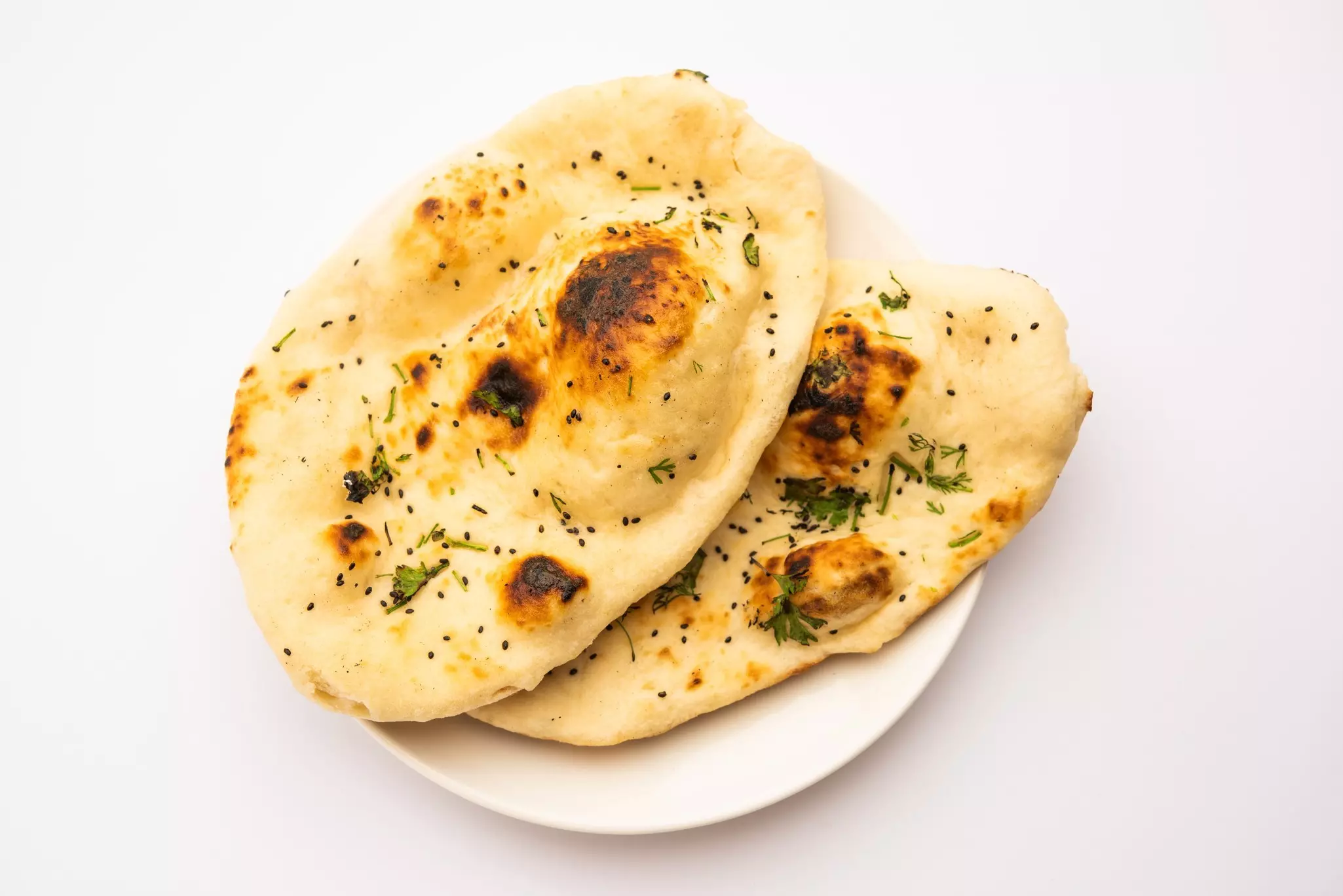 Two pieces of naan bread flecked with green and brown spices, resting on a  white plate