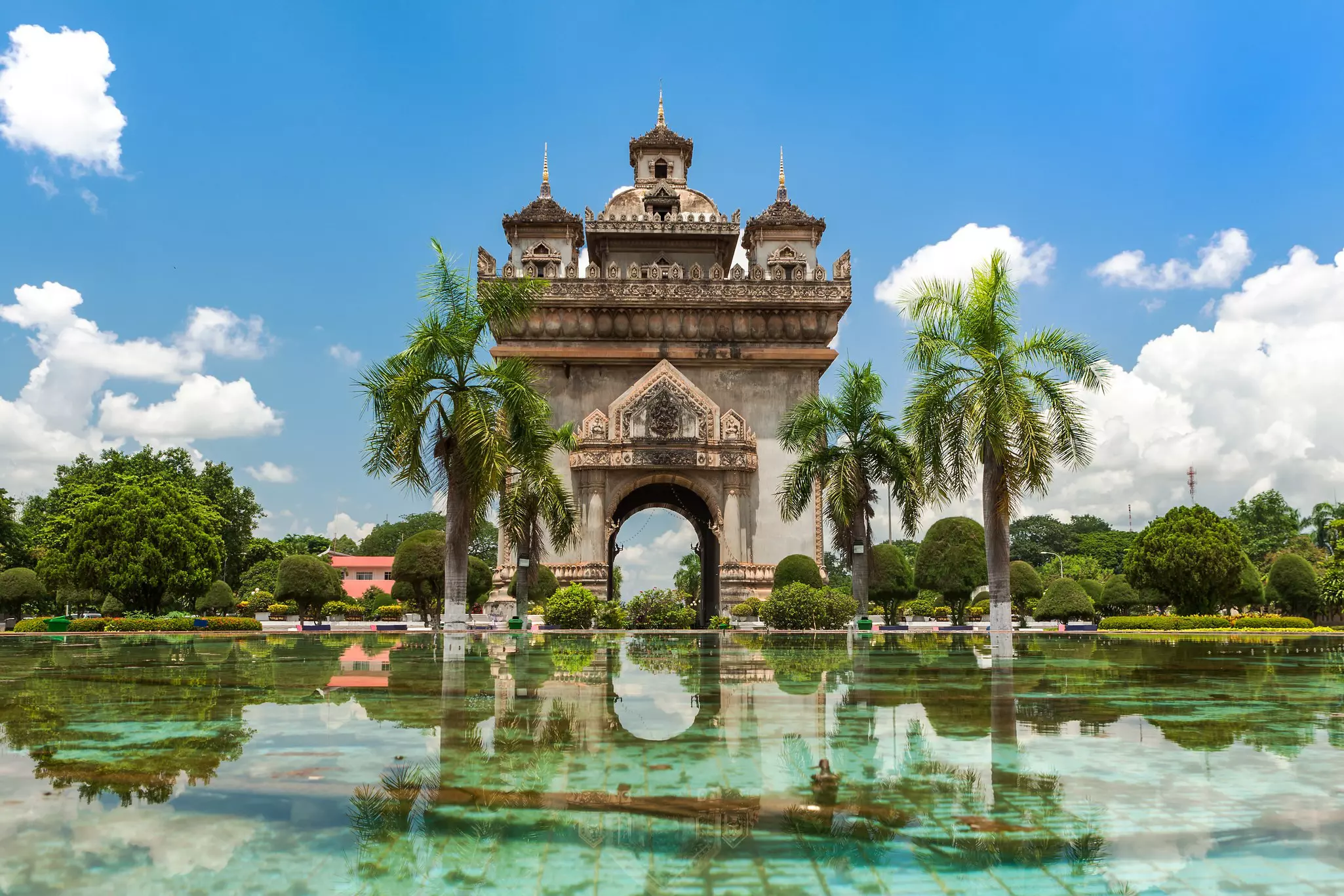 A large stone arch surrounded by a water feature and palm trees.