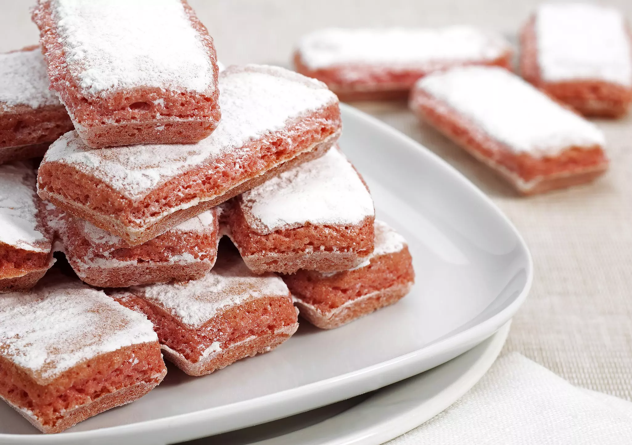 A platter of pink biscuits coated with powdered sugar.