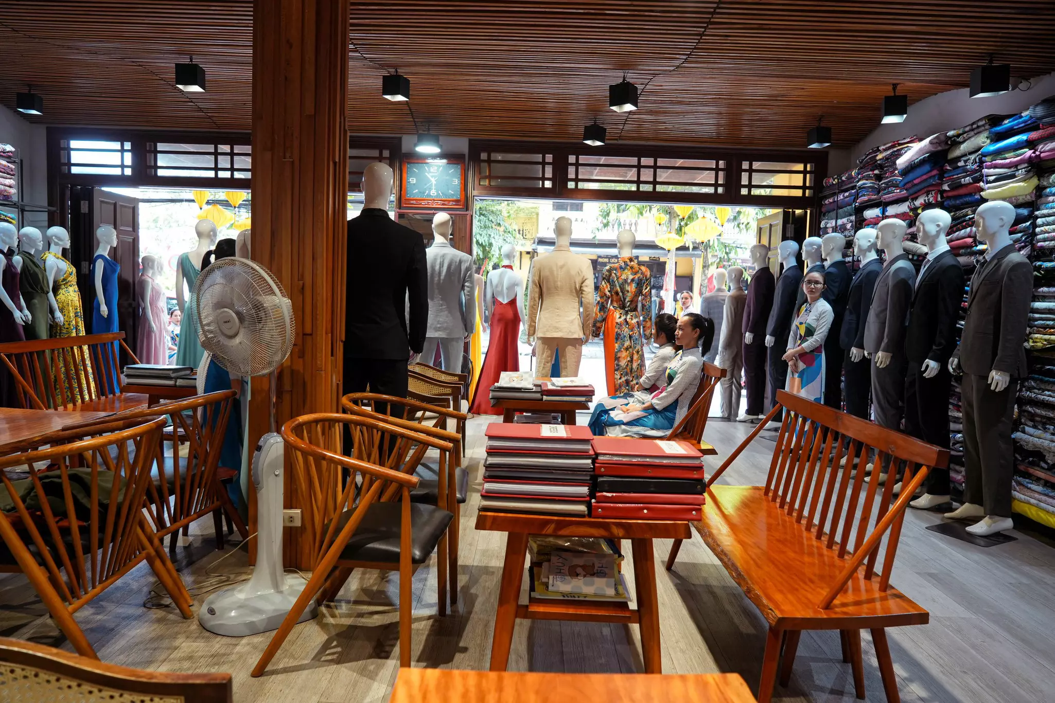 The showroom of a tailor with tables, mannequins and bolts of fabric on shelves against the walls.