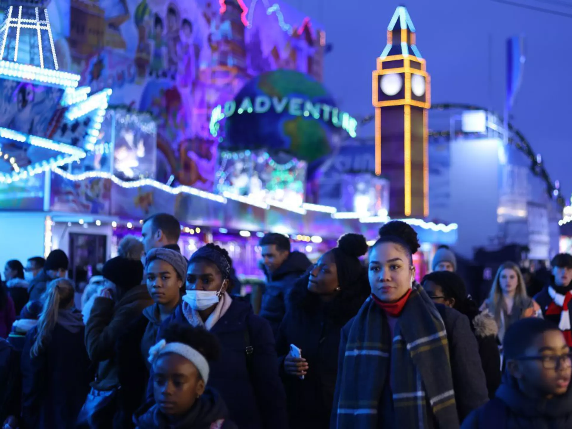 The outside of the London Review Bookshop. It's raining and a child walks past with a green umbrella. The inside of the store is lit up in a warm yellow and there are customers inside.