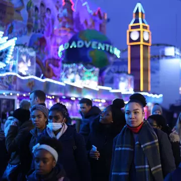 The outside of the London Review Bookshop. It's raining and a child walks past with a green umbrella. The inside of the store is lit up in a warm yellow and there are customers inside.