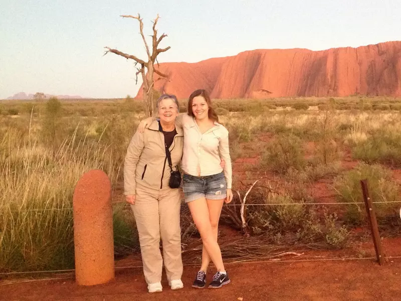 Two women smiling and laughing for the camera with Uluru rock in the background