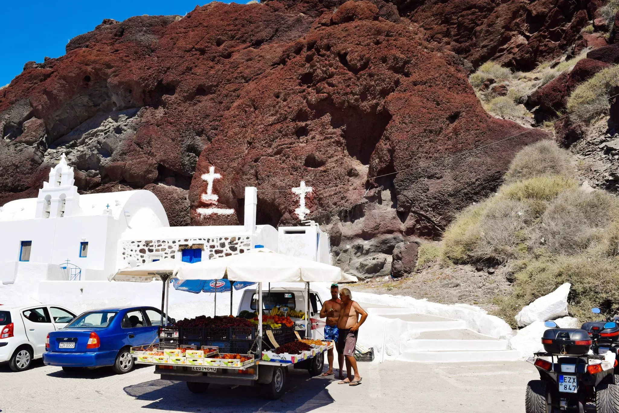A fruit and veg trailer attached to a van. An umbrella covers the produce while two men survey it.