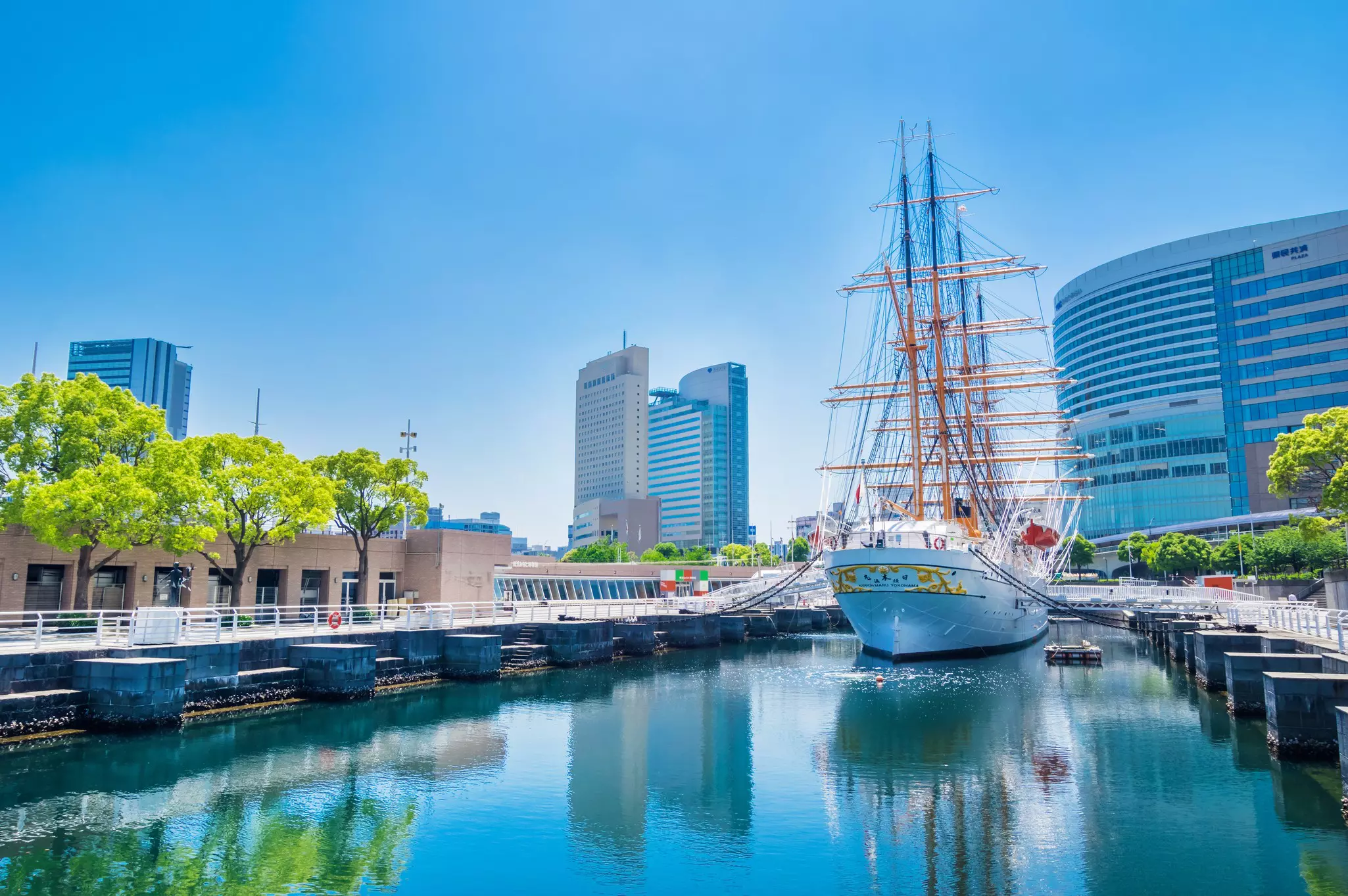 Wide shot of old sailing boat moored at in a canal with city buildings in the distance on a sunny day.