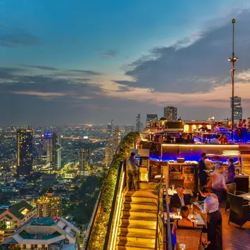 A view of a rooftop bar overlooking the skyline of a huge city at dusk.