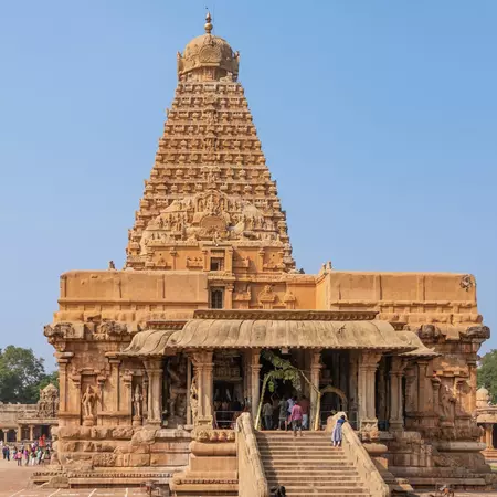 An ancient rock temple with an ornate stone facade comprising statues against a blue sky