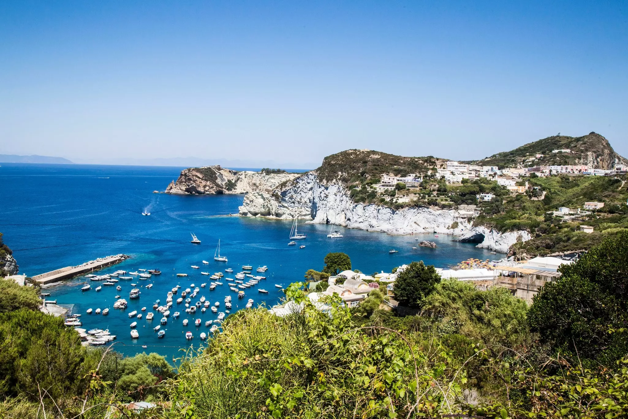 A wide view of a cove ringed with limestone cliffs and filled with moored boats.