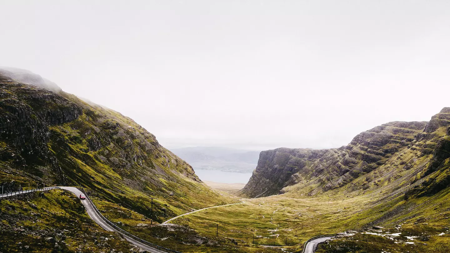 A hugely winding road weaves through hilly landscape on a foggy day