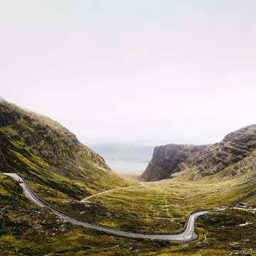 A hugely winding road weaves through hilly landscape on a foggy day