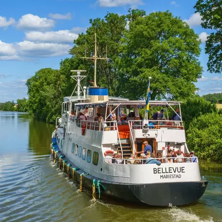 A boat with people sails through a canal on a sunny summer day.