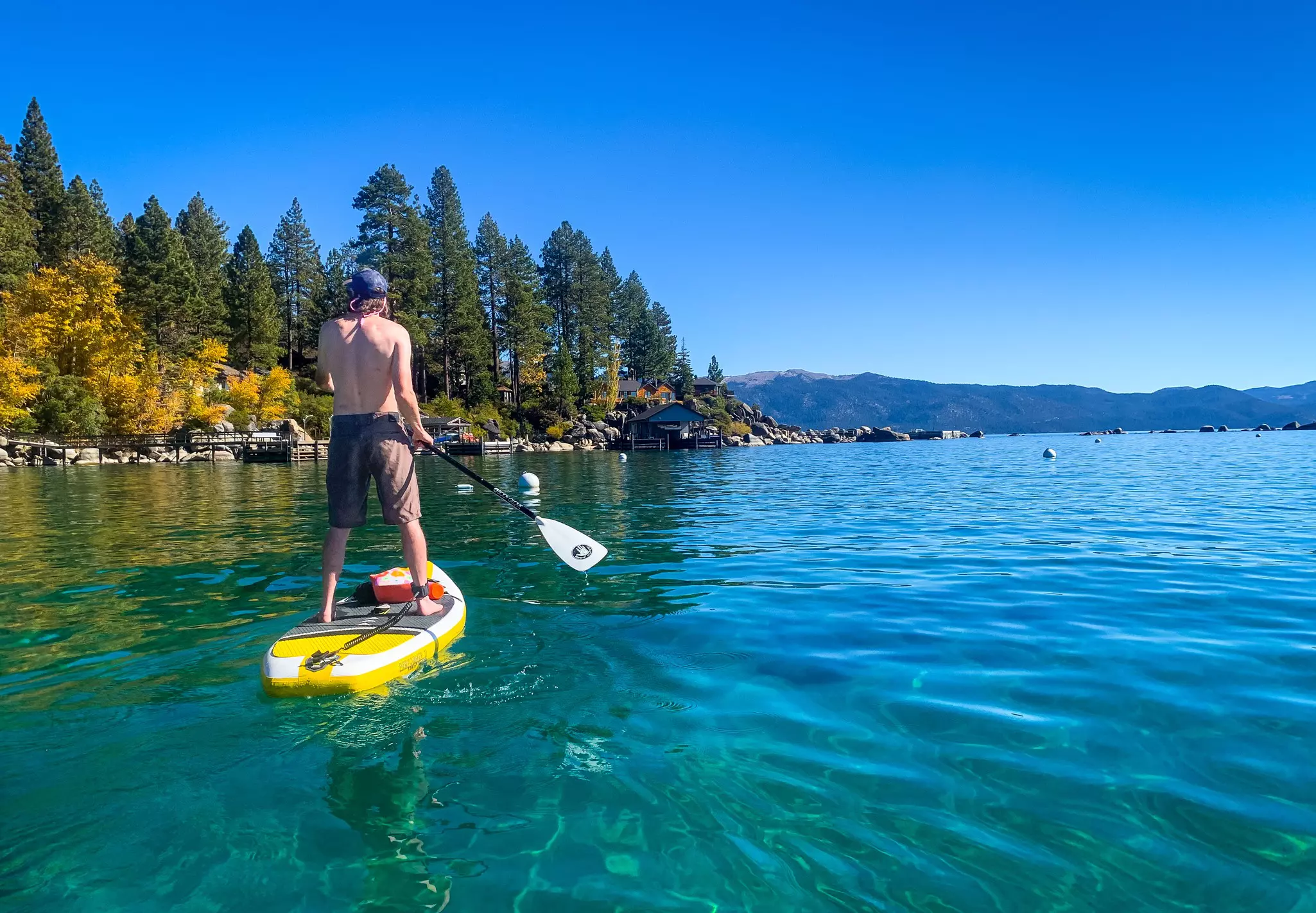 A person stands on a paddleboard on a clear lake with evergreens on the shore.