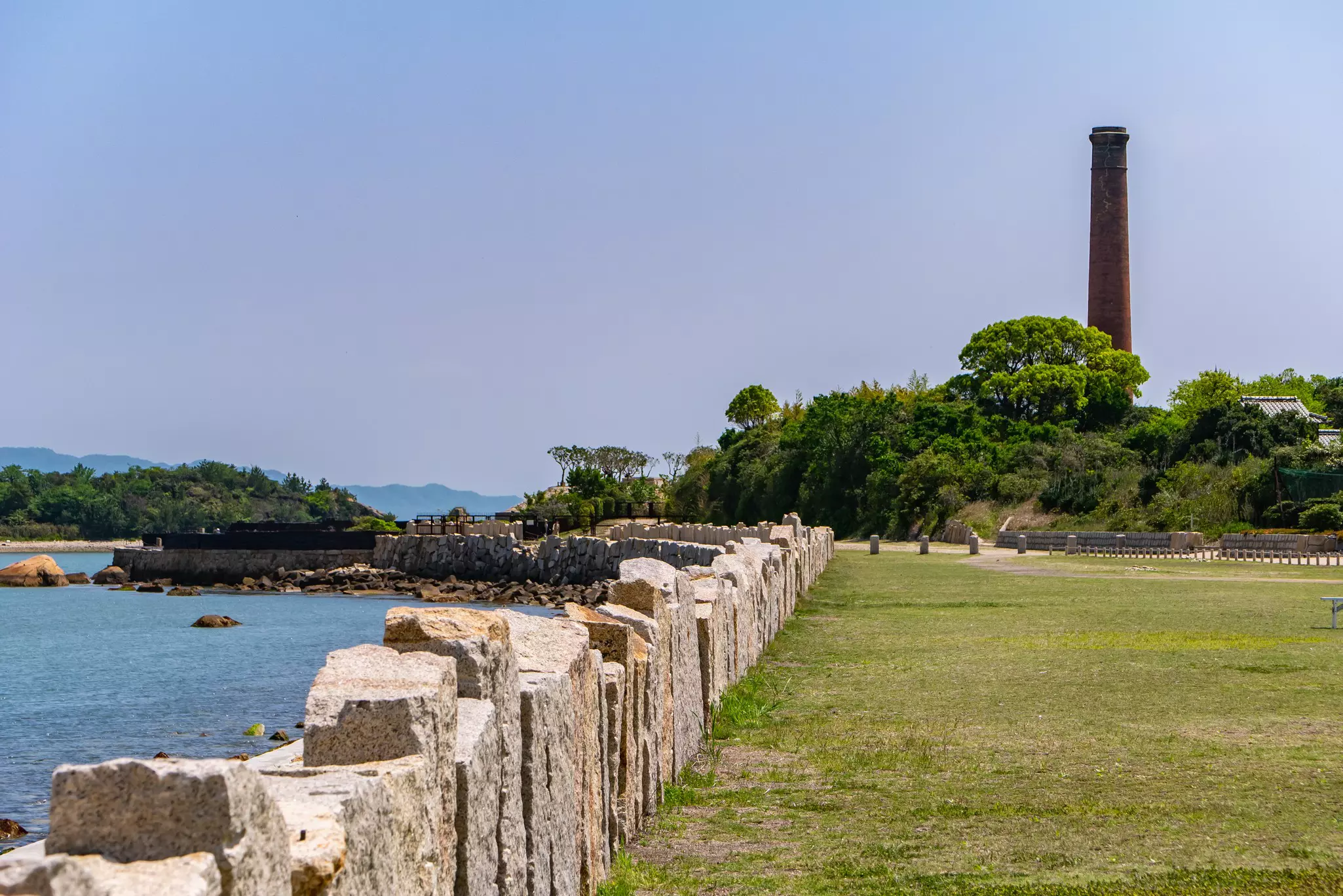 A large brick chimney rises above trees near the edge of an island.