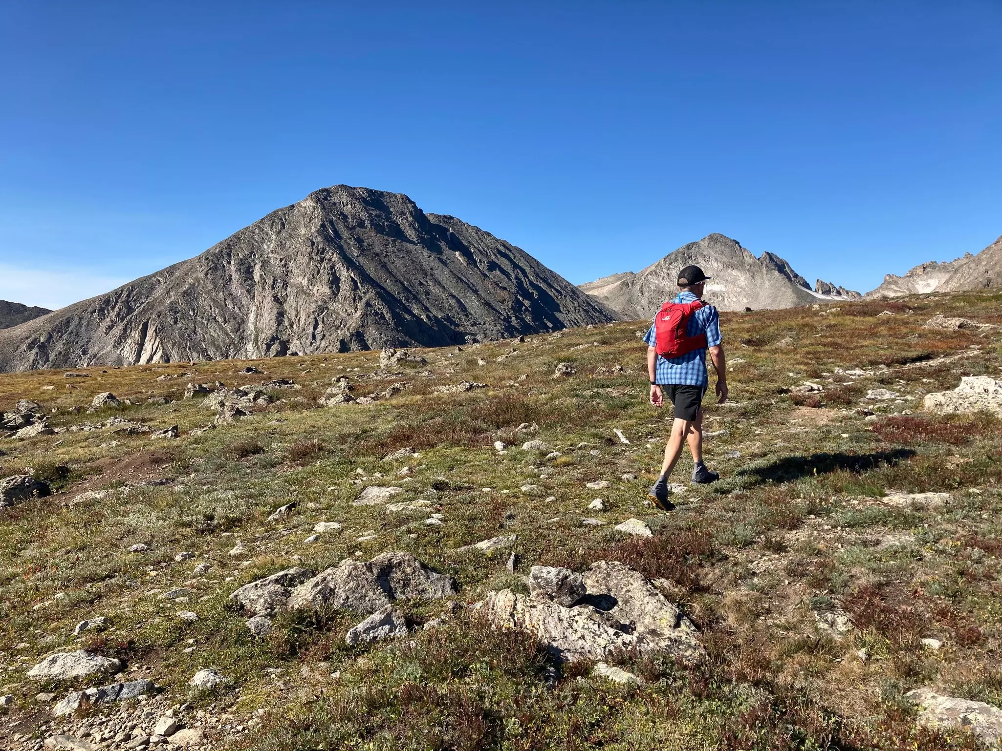 A hiker with a red backpack is seen from behind on a rocky slope.