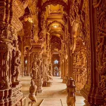 A long wooden corridor inside the Sanctuary of Truth in Pattaya, lined with intricately carved figures and columns.