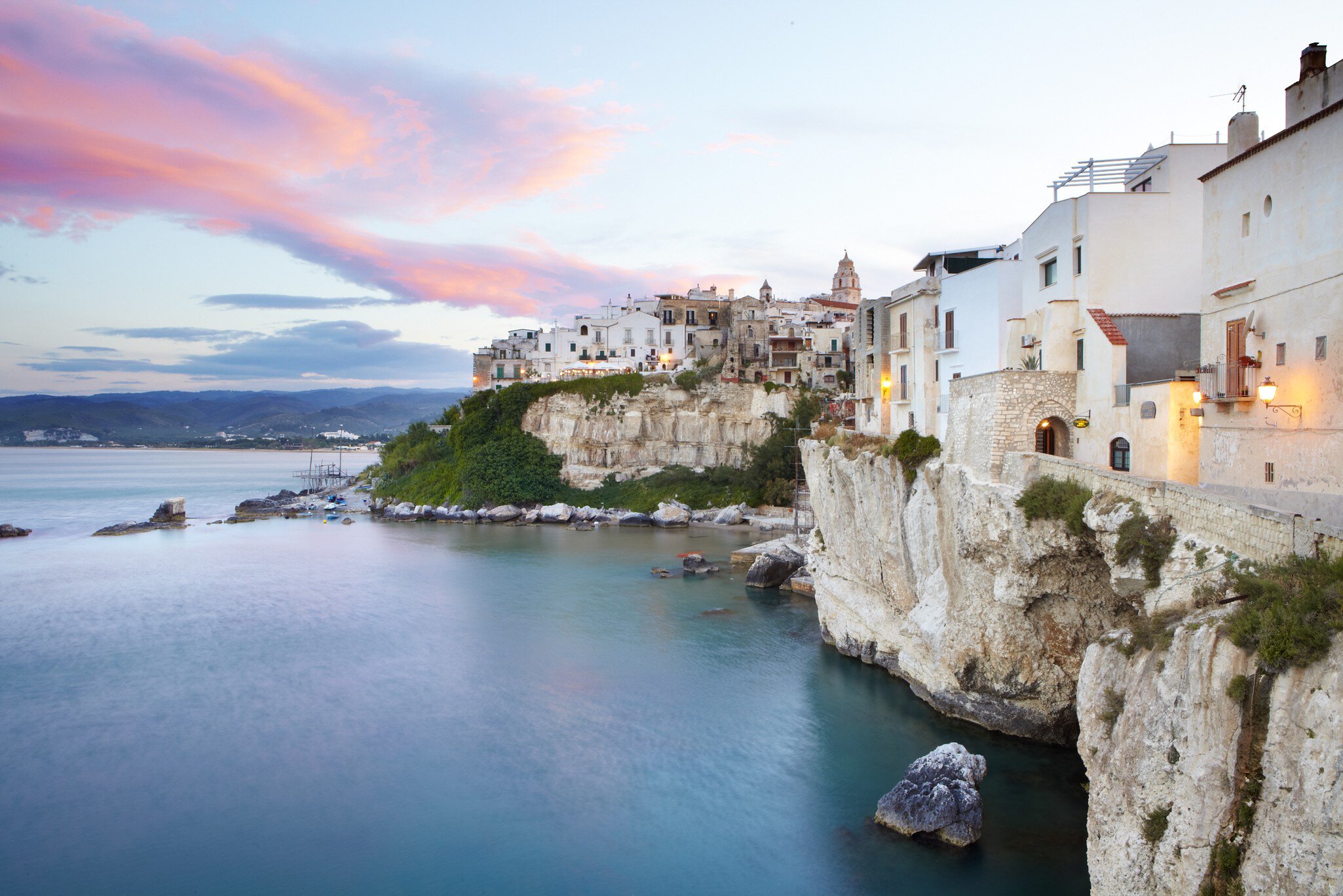 Sun setting on medieval town of Vieste perched on cliff ridge.