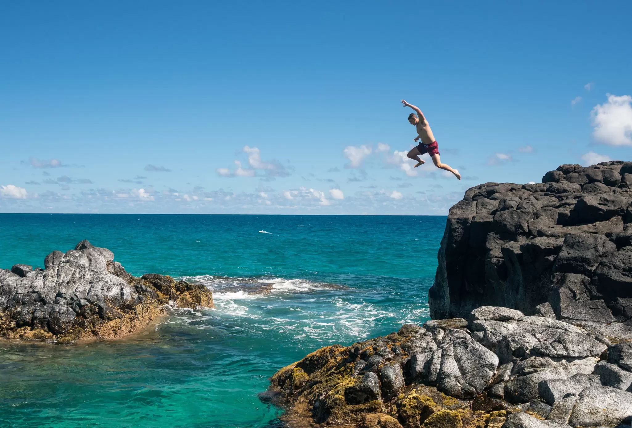 Man jumps off of a cliff into the ocean in Kauaʻi