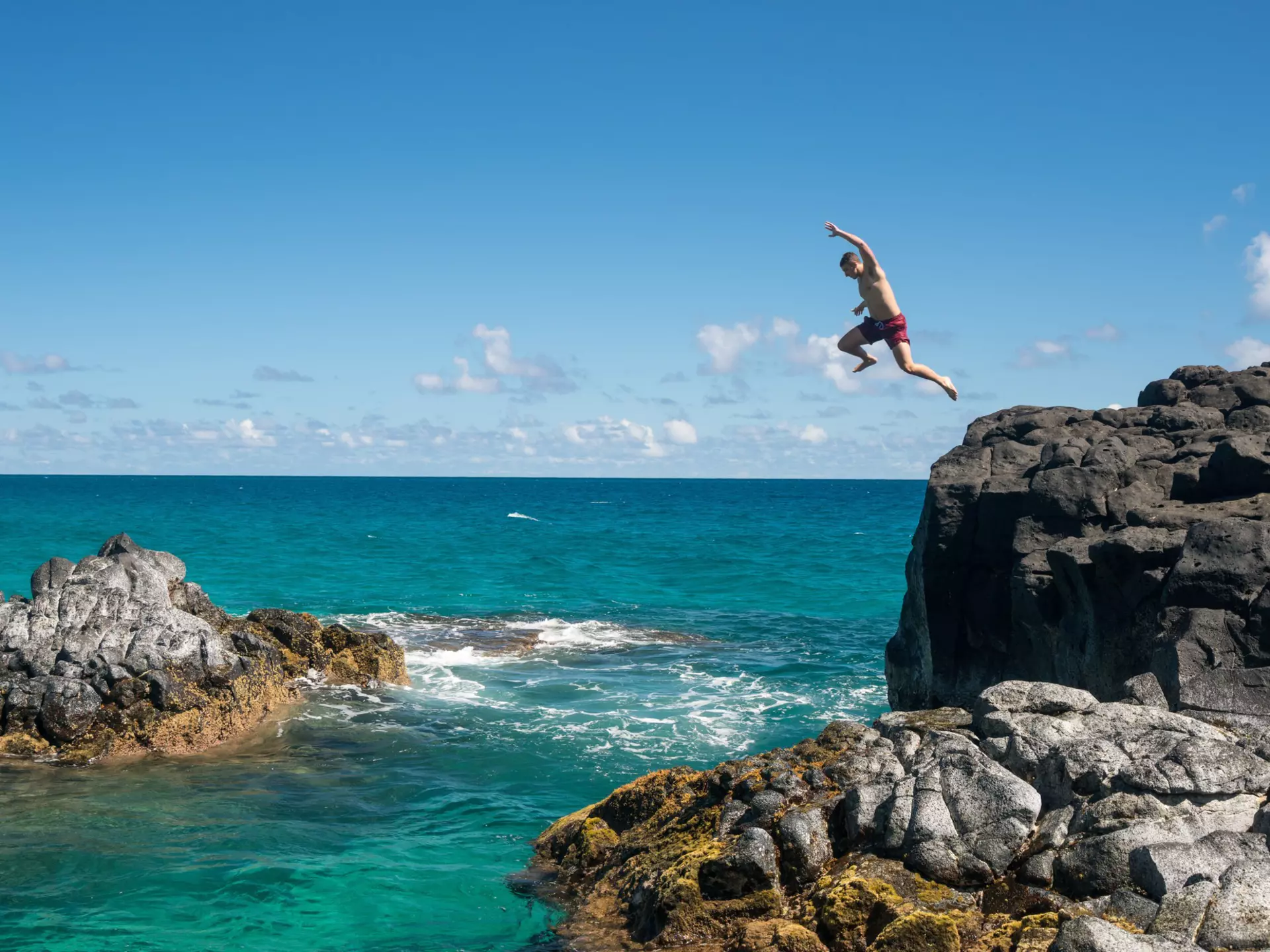 Man jumps off of a cliff into the ocean in Kauaʻi