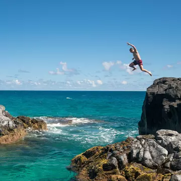 Man jumps off of a cliff into the ocean in Kauaʻi