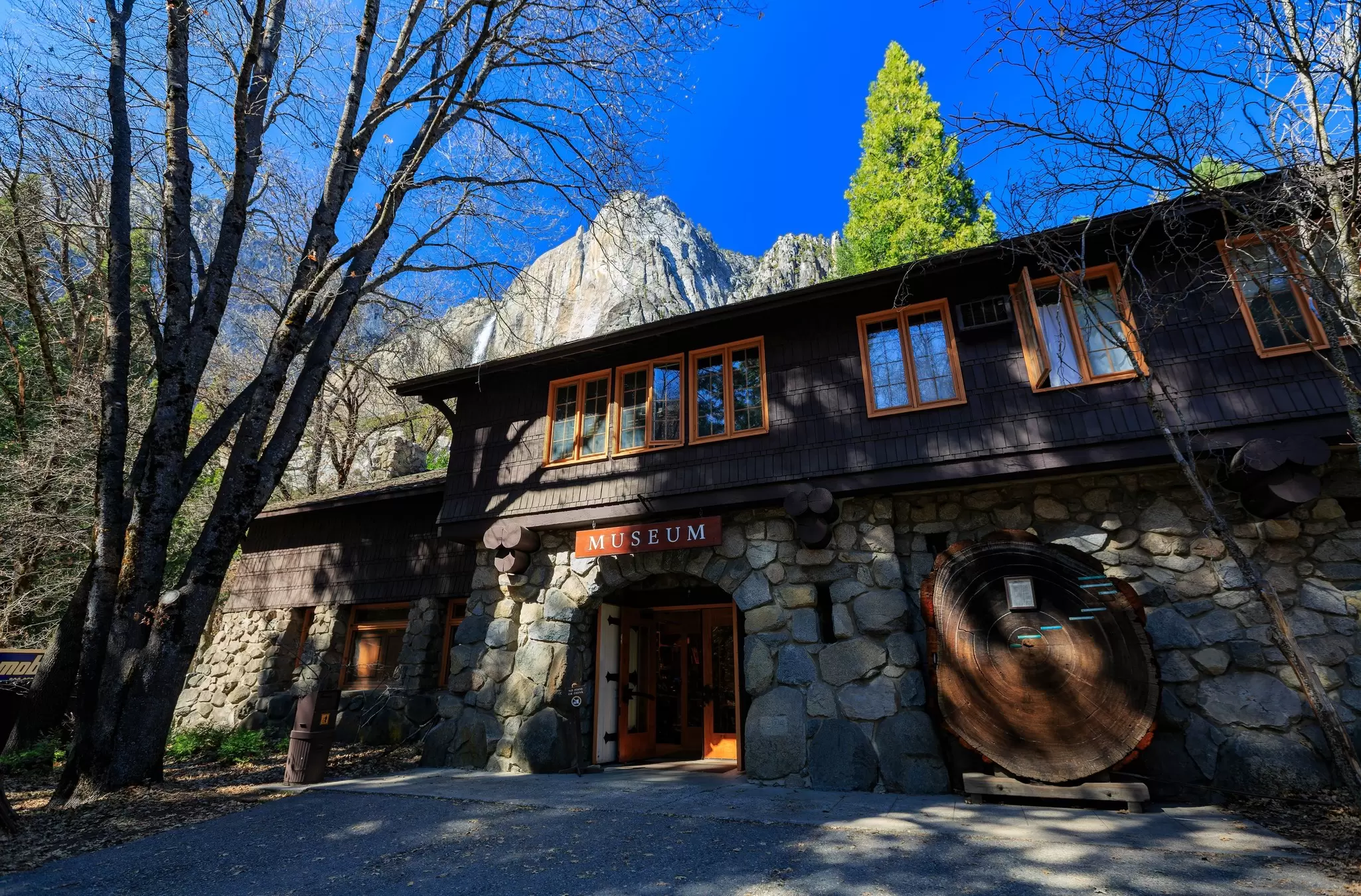 The stone and timber Yosemite Museum building in Yosemite Valley with granite cliffs rising behind