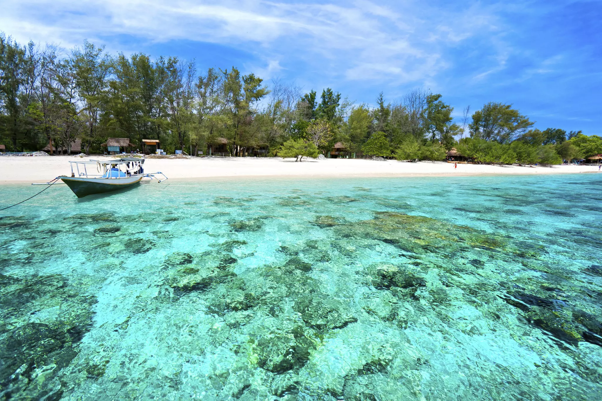 A boat docks in clear water at a beach in Indonesia.